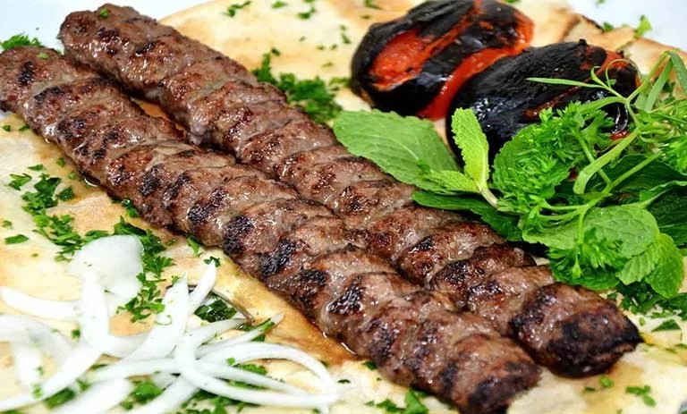 Two grilled koobideh kabobs with charred tomatoes, herbs and flatbread